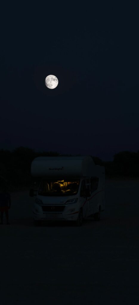 Autocaravana blanca iluminada por dentro bajo una luna llena de noche