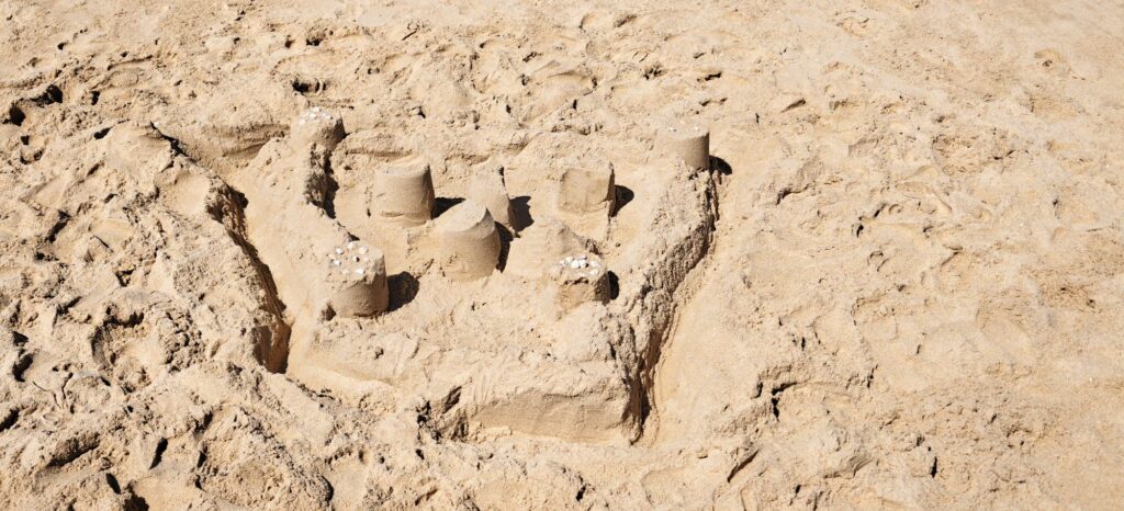 Castelo de area con sete torres cilíndricas coroadas con cunchas pequenas, unha muralla e un foxo
