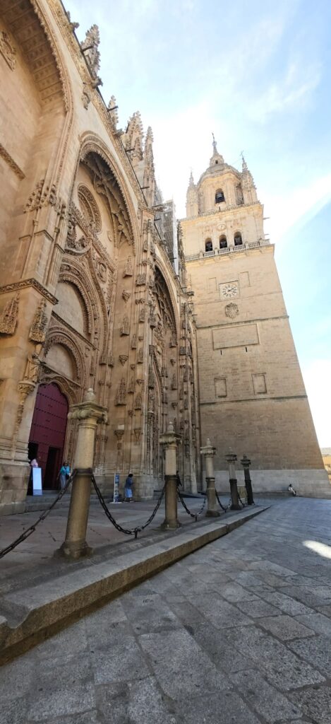 Fachada occidental de la Catedral Nueva que se eleva hacia la torre, con postes de piedra y cadenas delante