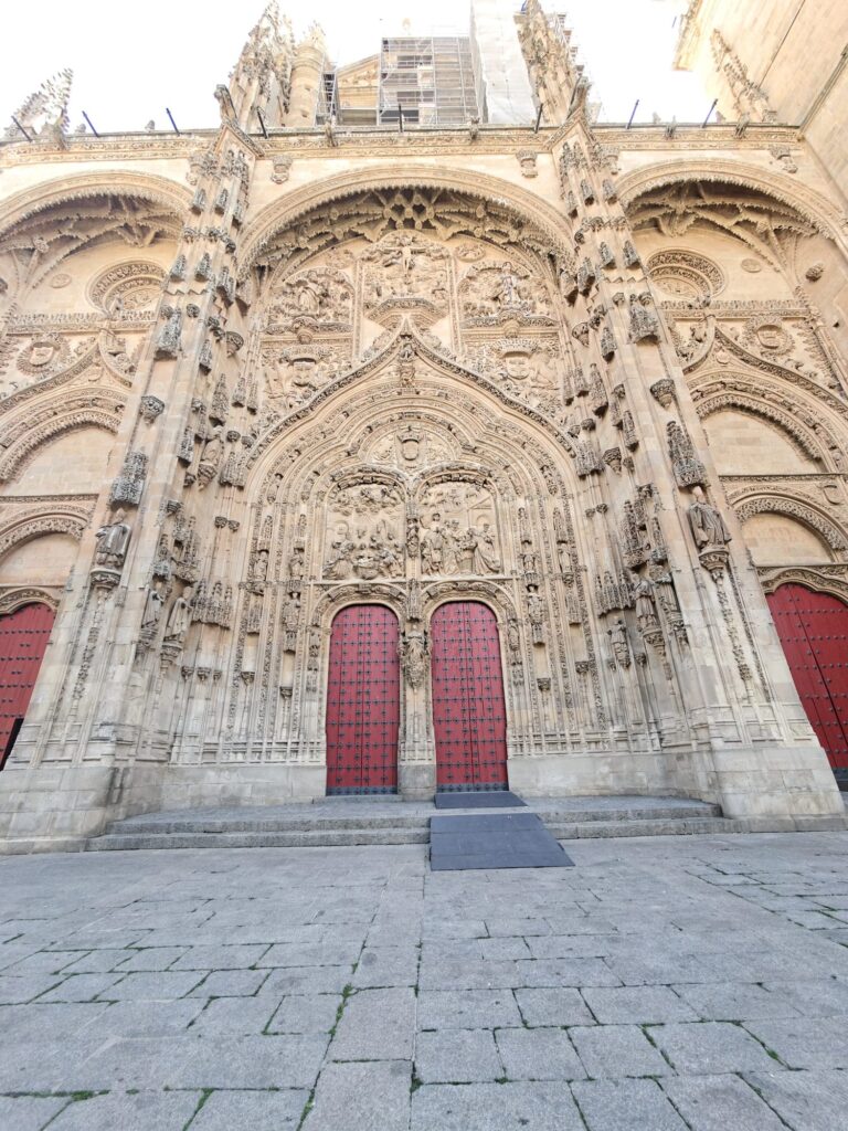Fachada ocidental da Catedral Nova de Salamanca com andaimes na parte de cima e portas vermelhas em baixo