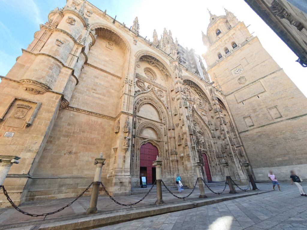 A Catedral Nova de Salamanca em contrapicado, com portais esculpidos, a torre, pilares de pedra e correntes