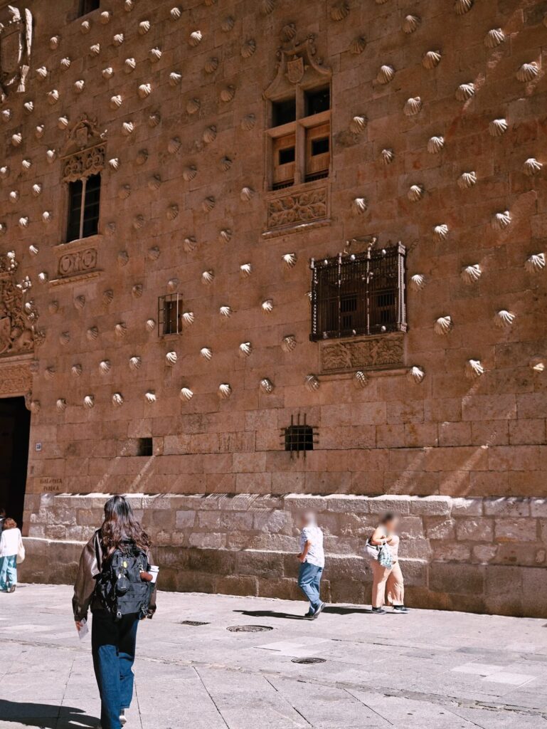 Pessoas a passar junto à Casa de las Conchas, em Salamanca, um muro de arenito coberto de conchas esculpidas