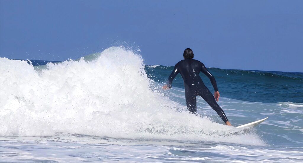 Surfista visto de espaldas alejándose de la cámara mientras la ola se deshace a su izquierda