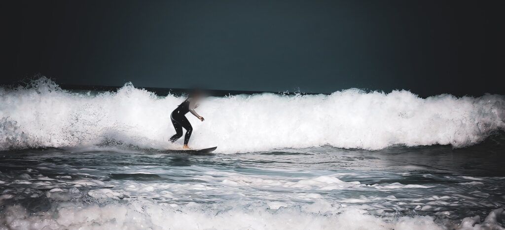 Surfista deslizándose ante una larga pared de espuma blanca sobre un cielo muy oscuro
