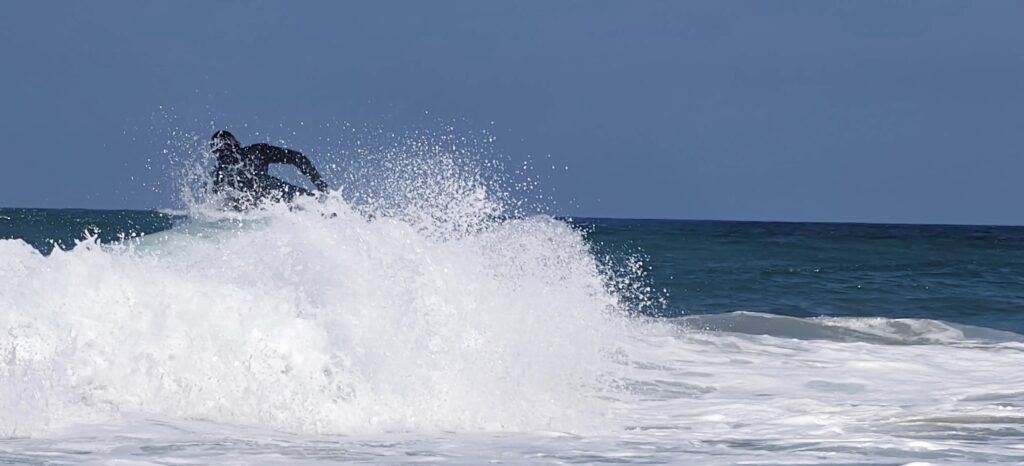 Surfista casi oculta dentro de una explosión de espuma blanca al romper la ola